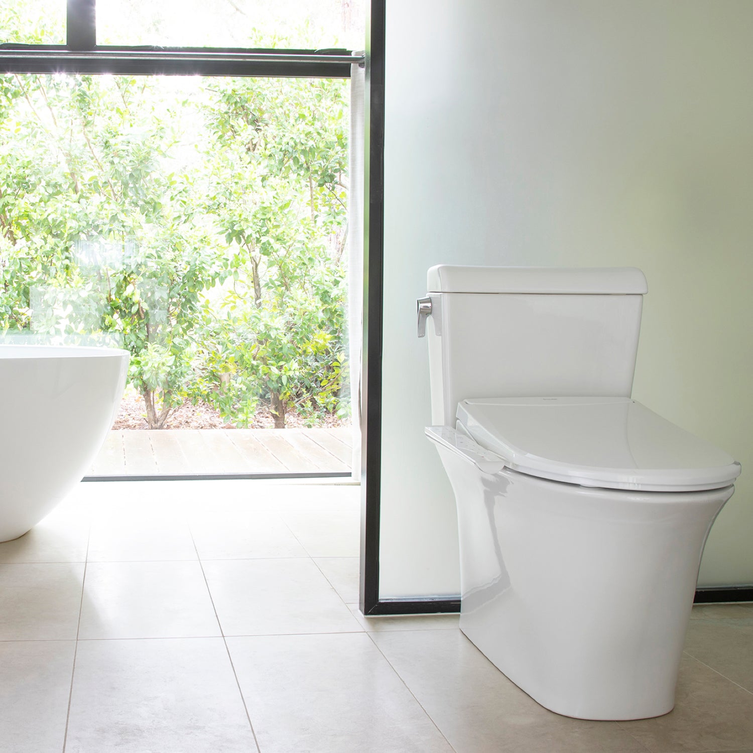 Modern white toilet with Brondell Swash Thinline T22 electric bidet installed in a bright bathroom with a window view of greenery.